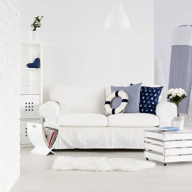 Salon w kolorze białym z białą kanapą i morskimi dodatkami, styl marynistyczny. Element charakterystyczny: biala kanapa z morskimi dodatkami
