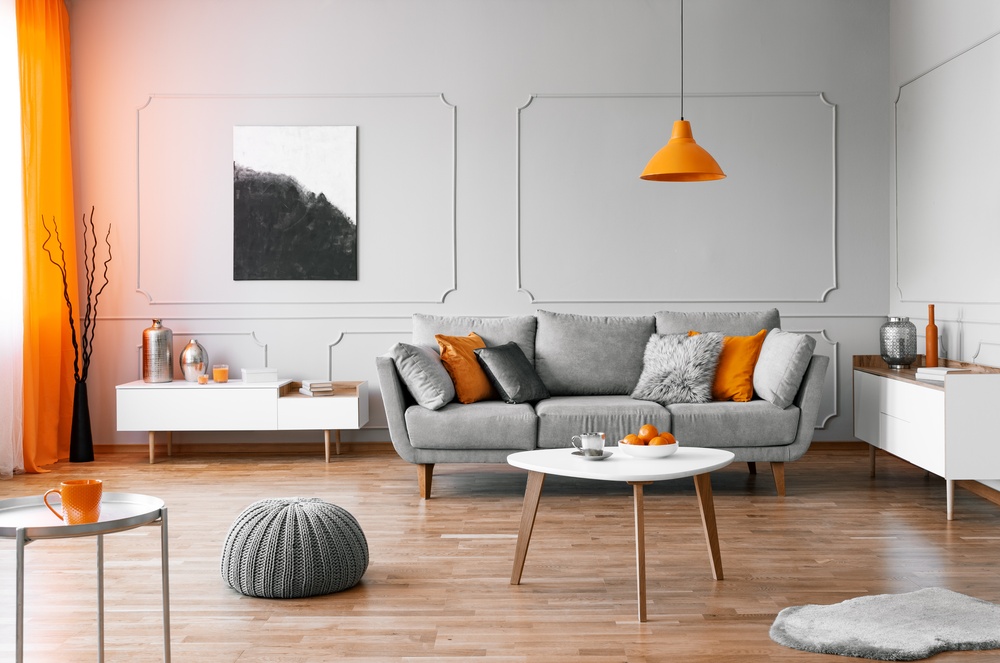 Salon w stylu minimalistycznym z szarą kanapą i pomaranczowymi dodatkami