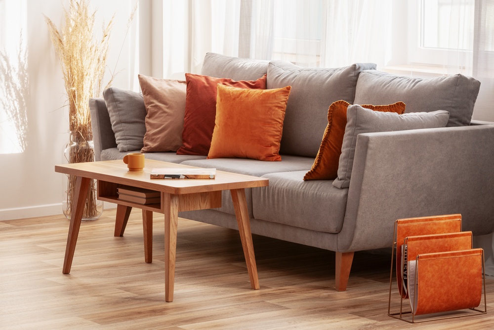 Salon w stylu skandynawskim z szarą kanapą z pomarańczowymi poduszkami.
