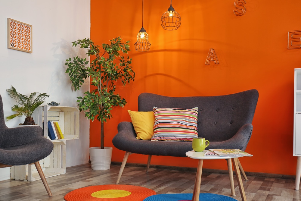Salonw  stylu vintage z szarą kanapą na pomarańczowej ścianie