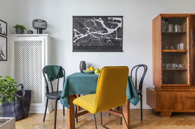 Salon w kolorze szarym z kolorowymi krzesłami i zabudowanym kaloryferem, styl vintage. Element charakterystyczny: kolorowe krzesłai i zabudowany kaloryfer