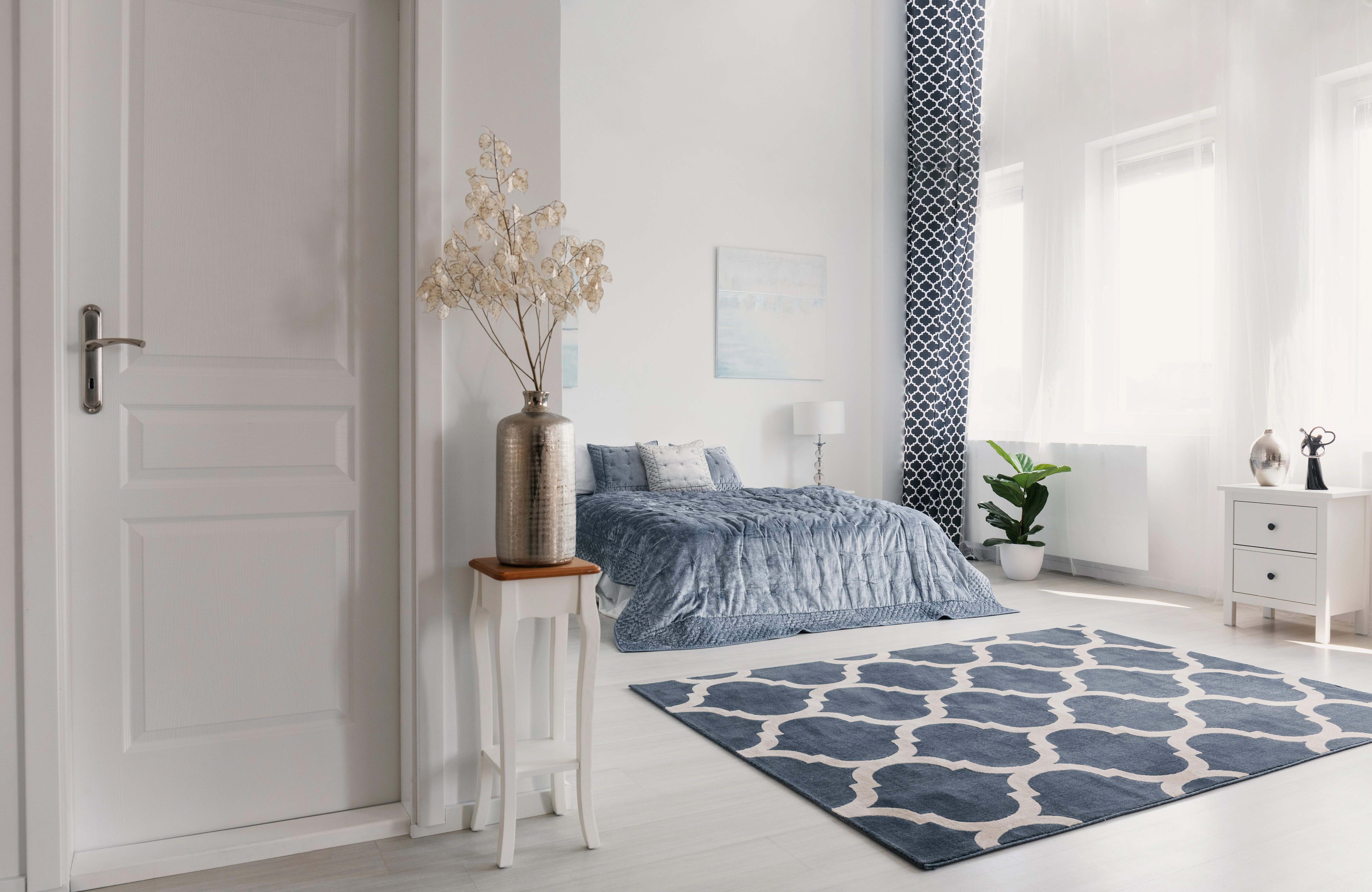 Inspiracja prezentująca sypialnię w kolorze białym z łóżkiem z niebieskimi dodatkami, styl nowojorski. Element charakterystyczny: łóżko z niebieskimi dodatkami