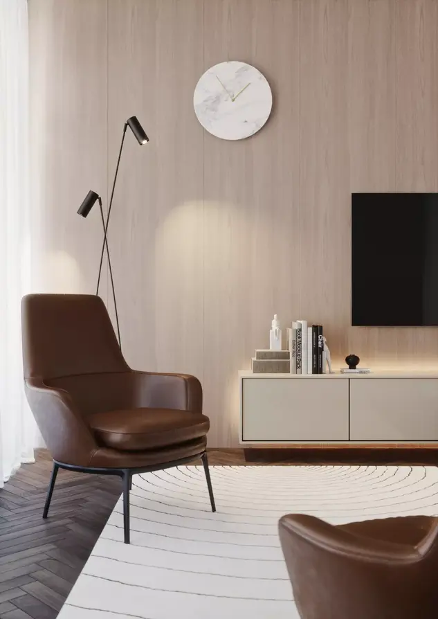 Salon w stylu nowoczesnym w odcieniach beżu. Na ścianie zamontowany telewizor oraz pod telewizorem widoczna beżowa komoda. Elementem uzupełniającym jest jasno-beżowy fotel.