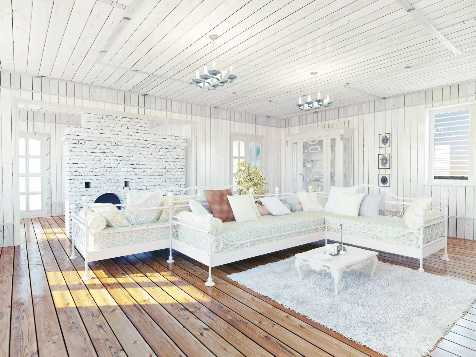 Salon w stylu prowansalskim w odcieniach beżu i bieli. Sofa z metalowymi wykończeniami i brązowa, drewniana podłoga.