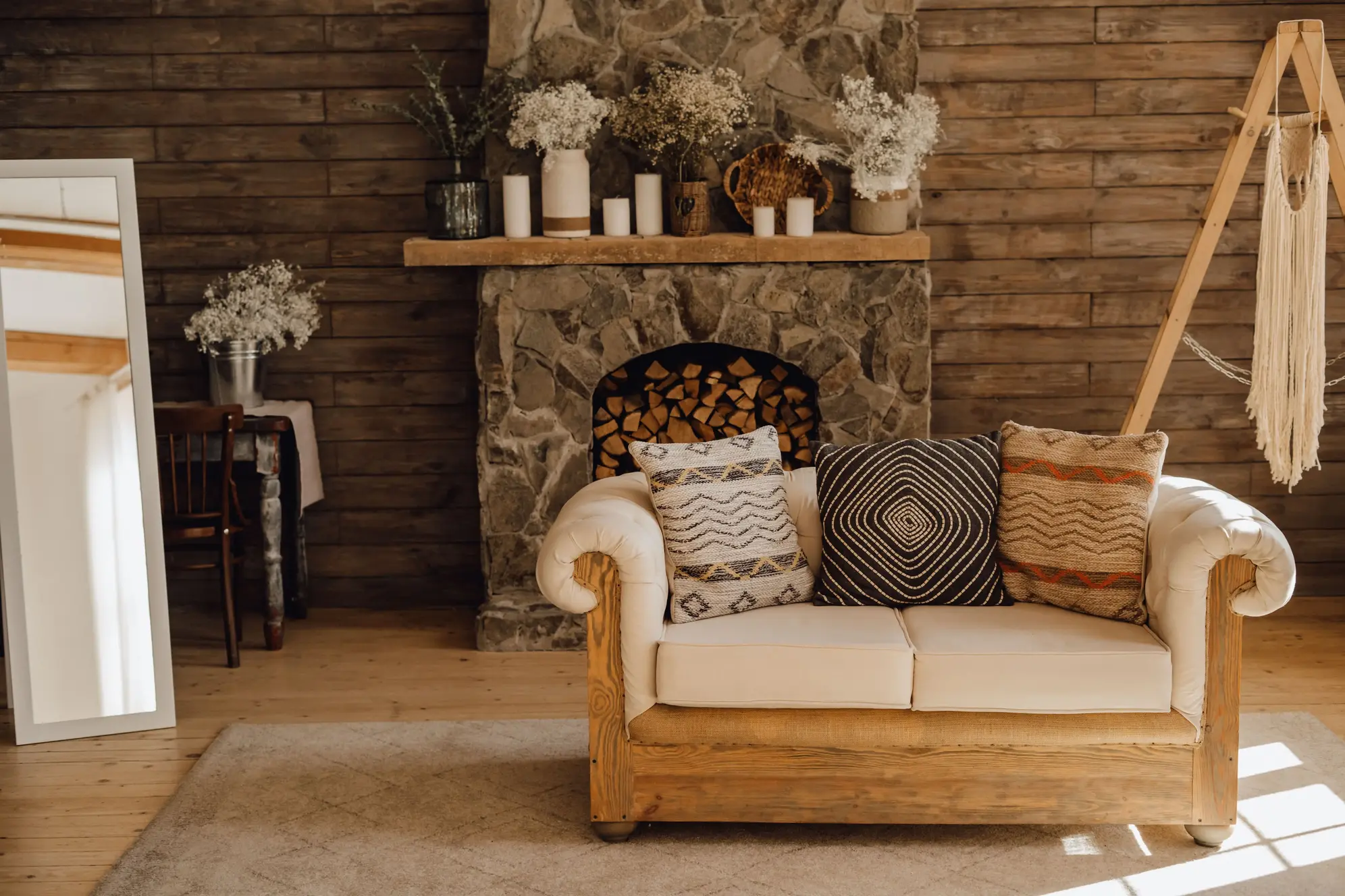 Salon w stylu rustykalnym z kamiennym kominkiem i dużym fotelem z ozdobnymi poduszkami.