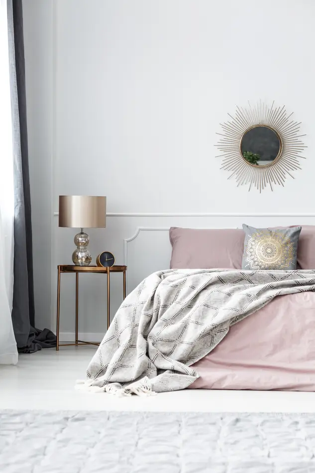 Sypialnia w stylu glamour w odcieniach bieli i różu z łóżkiem, złotą lampą i zdobieniami na ścianie