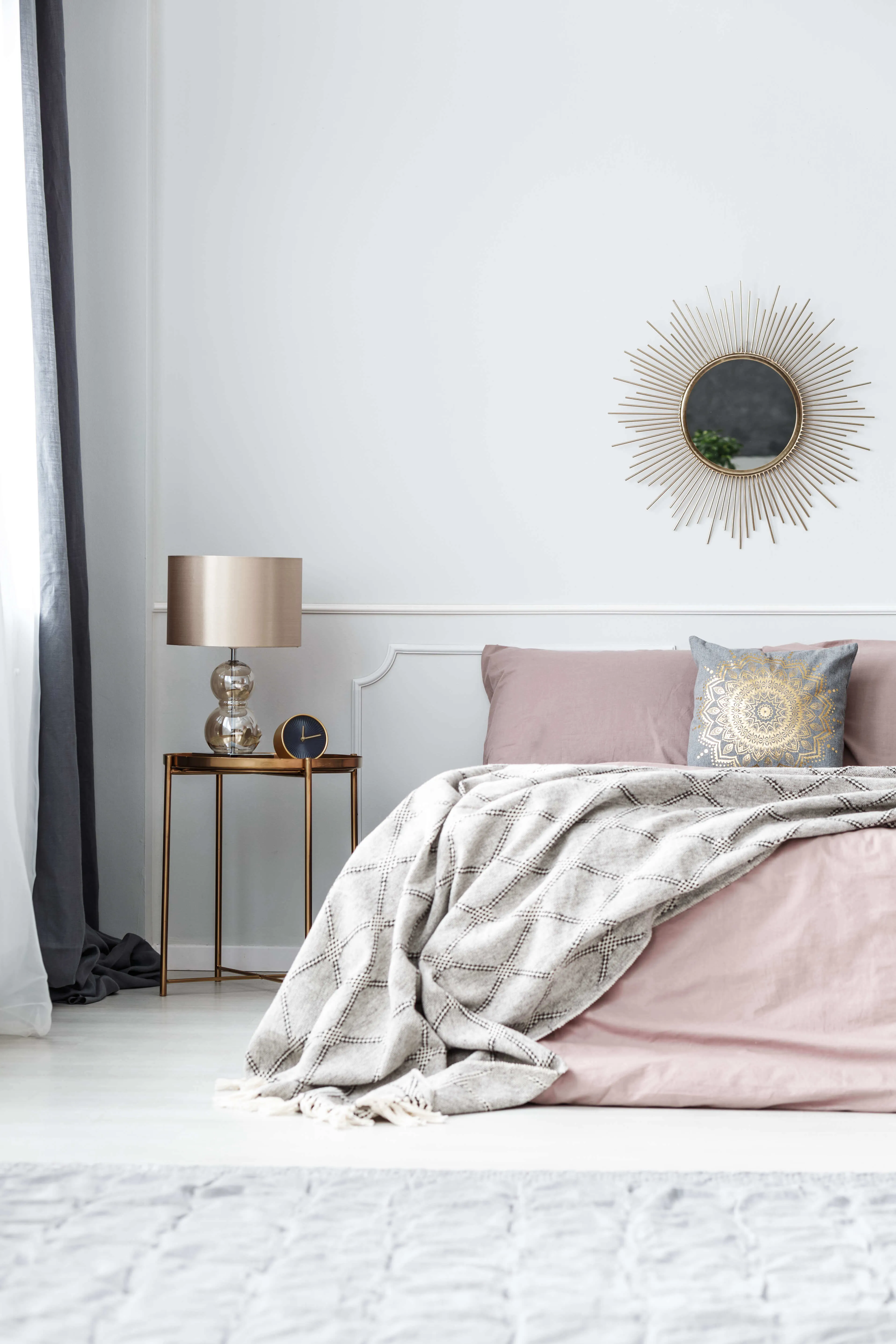 Różowa sypialnia w stylu glamour z dużym łóżkiem. Na ścianie złote lustro.