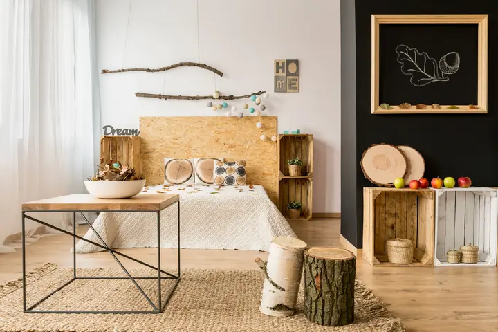 Sypialnia w stylu rustykalnym z dużym łóżkiem wykończonym drewnianymi elementami. Nad łóżkiem kolorowa girlanda z lamp.